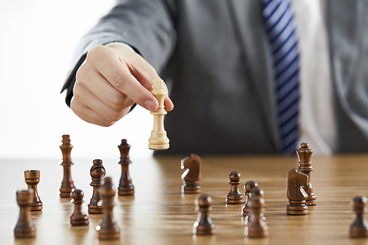 A businessman in a suit using his white king chess piece among dark chess pieces on a table - problem solving conce